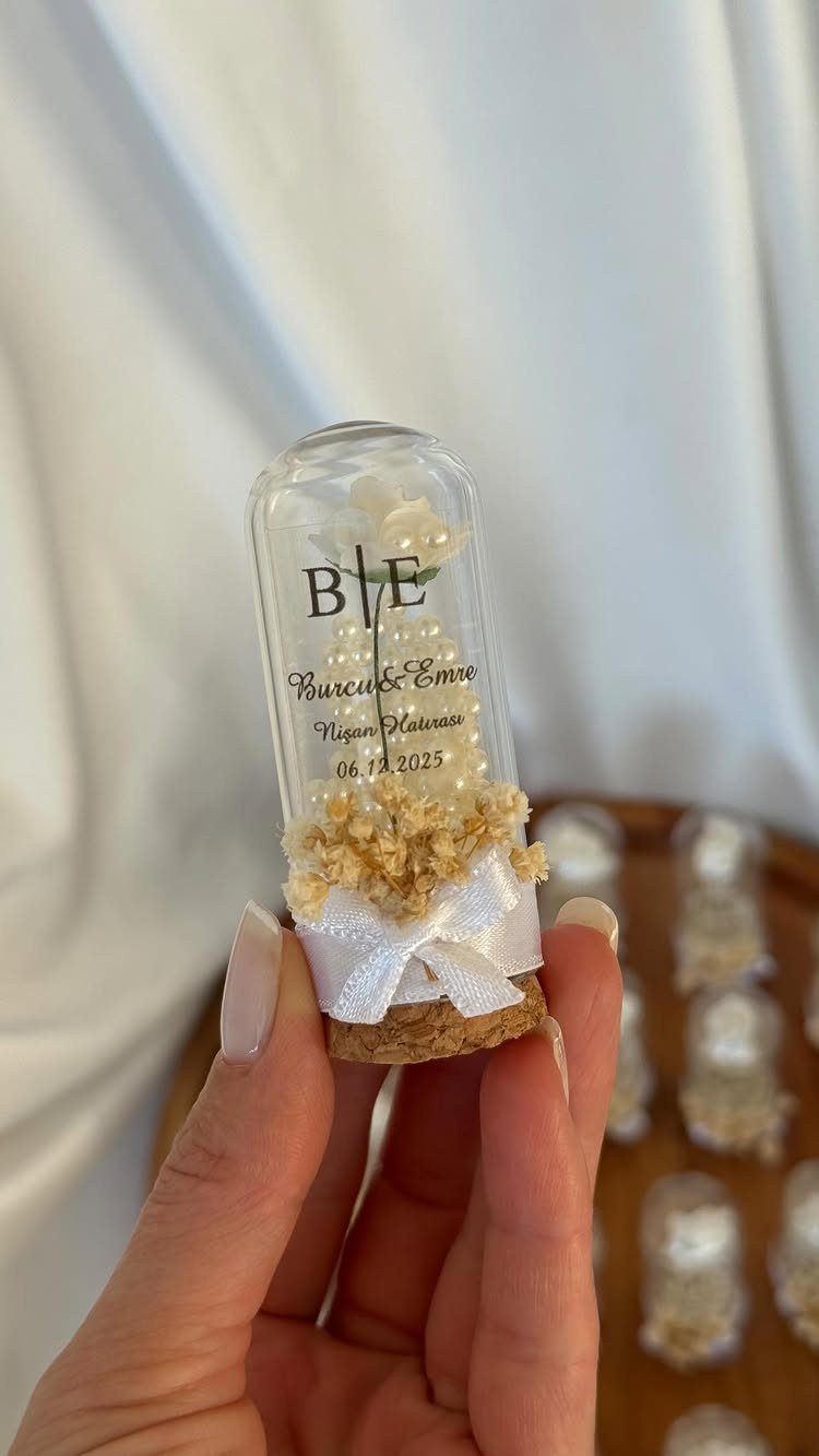 Small glass vial wedding favor with a white flower and ribbon bow.