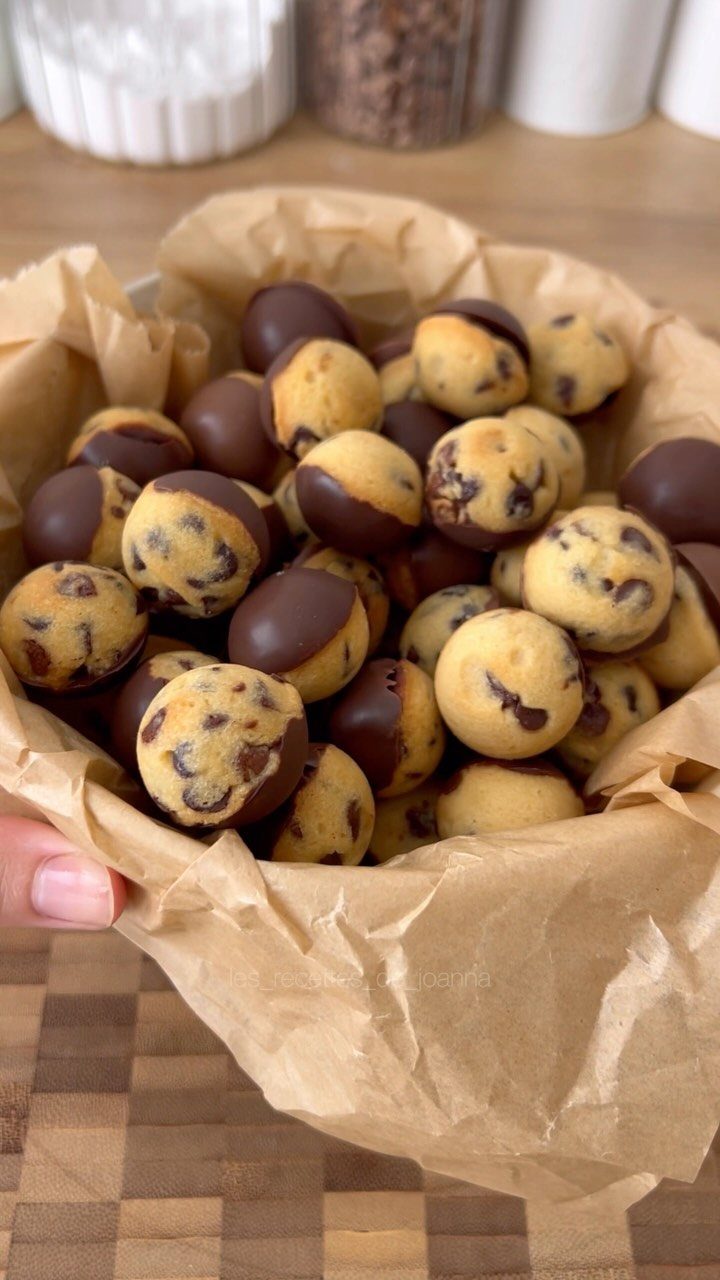 Chocolate chip cookie dough balls partially dipped in chocolate in a paper bowl