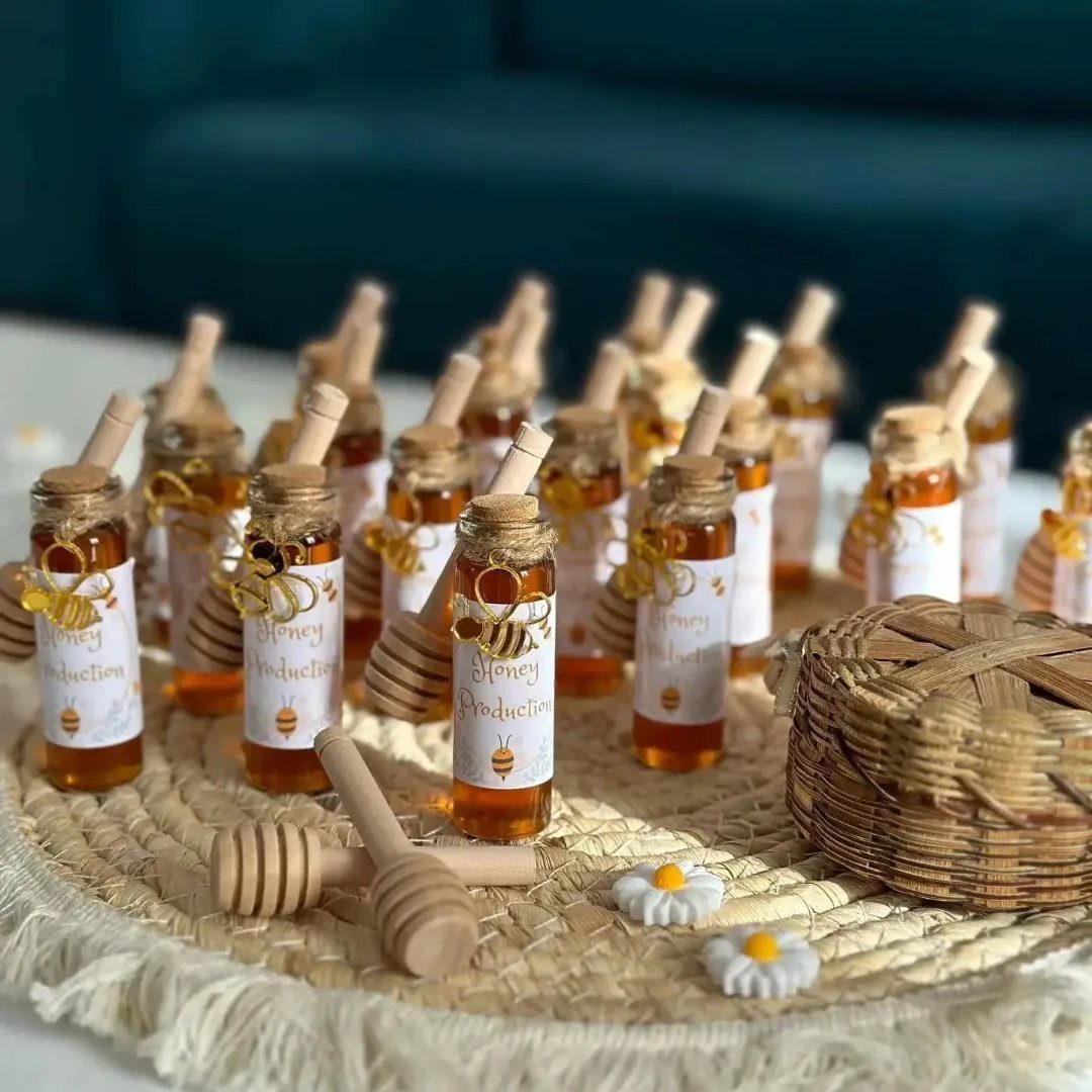 Small honey jars with wooden dippers and bee labels on a woven mat