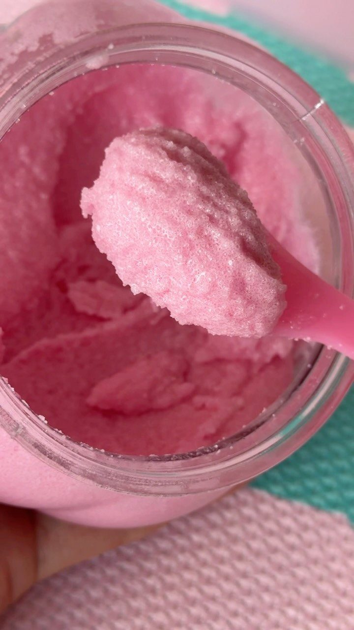 Pink sugar scrub in a glass jar being scooped with a pink spoon.