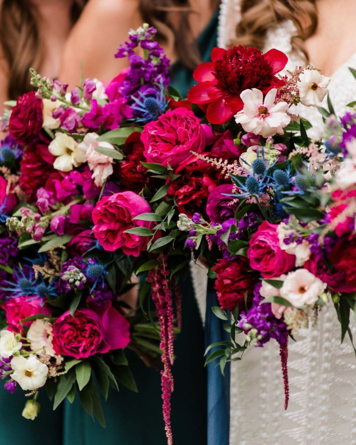 Jewel-toned floral bouquets with magenta roses and blue thistles held by wedding party.