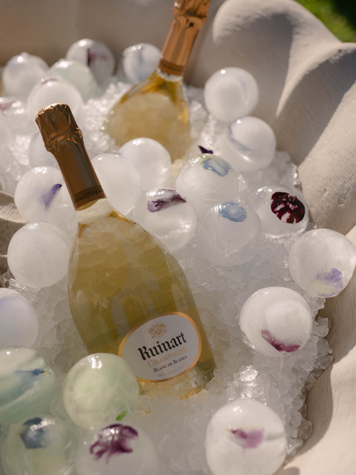 Champagne bottles chilled in ice with spherical ice balls containing purple flower petals.