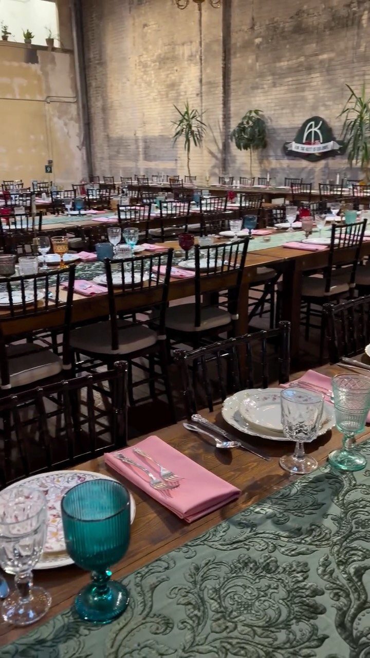 Wooden banquet tables with green damask runners, pink napkins, and teal glassware.