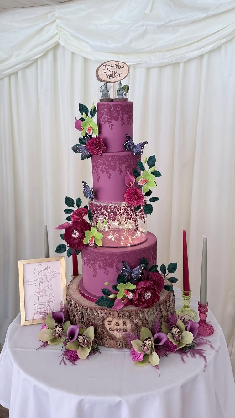 Purple multi-tiered wedding cake with magenta flowers and butterflies on a wooden base