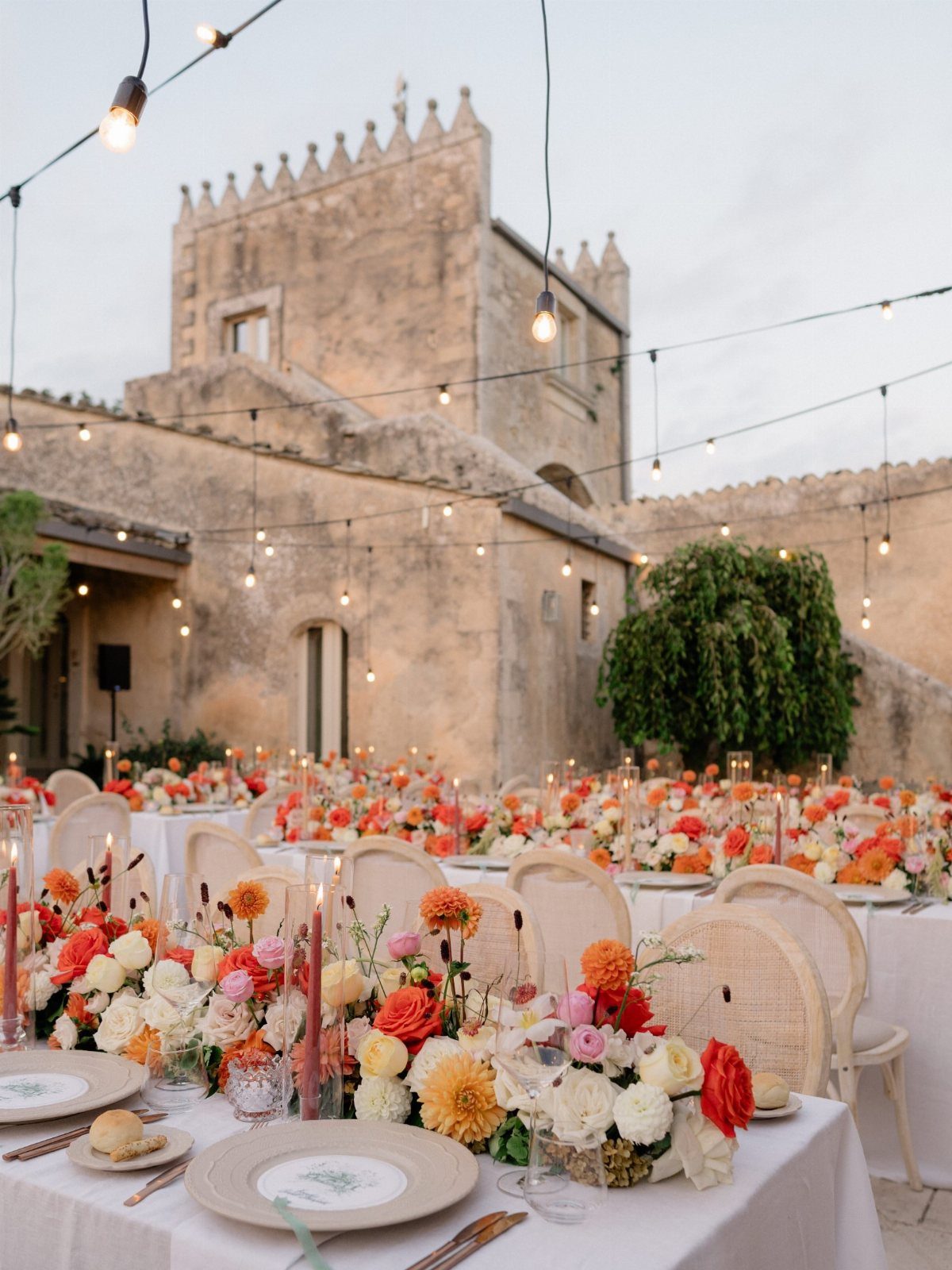 Wedding table with orange and yellow floral centerpieces before a rustic stone building.