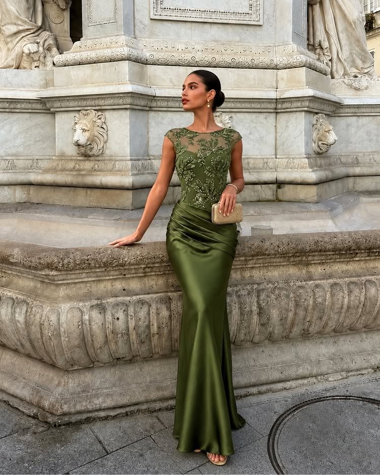 Woman in an olive green satin gown posing against a carved stone wall.