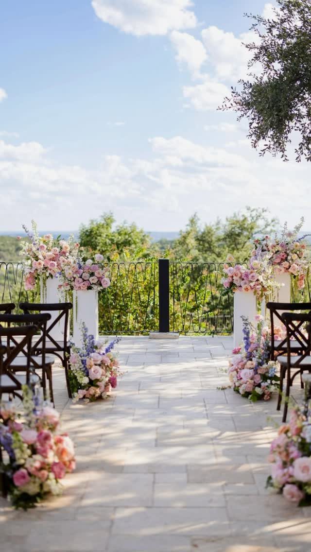 Outdoor wedding ceremony aisle with pink and purple floral arrangements on stone patio