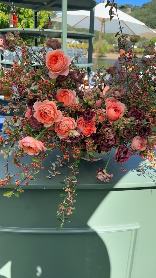 Coral roses and deep plum flowers in a lush outdoor wedding arrangement.