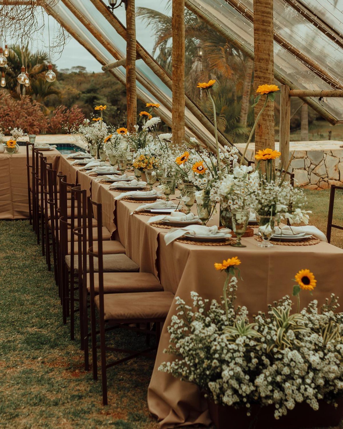 Long wedding table with tan linens and bright yellow sunflower floral arrangements.