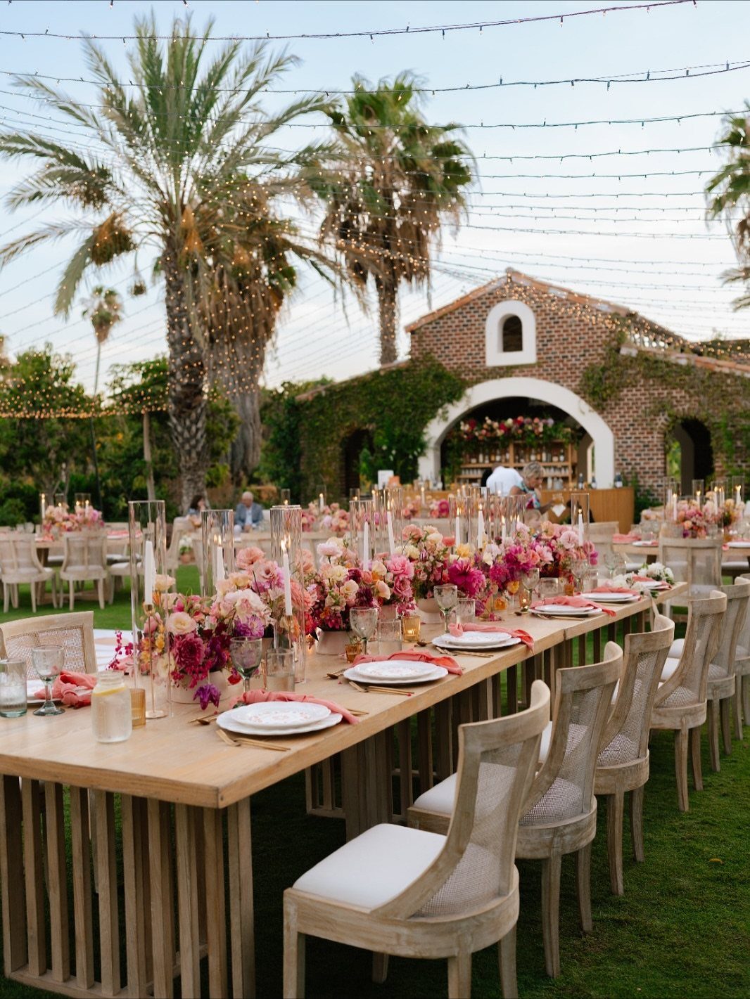 Long wooden wedding table with coral and lilac flowers on a green lawn.