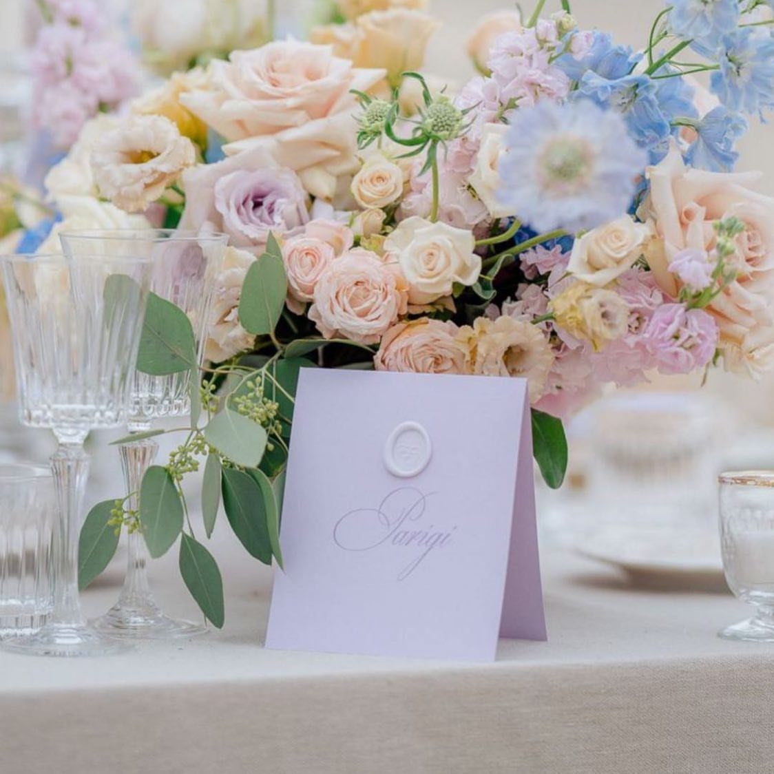Lilac, light blue, and pink floral centerpiece with a lilac place card on table.