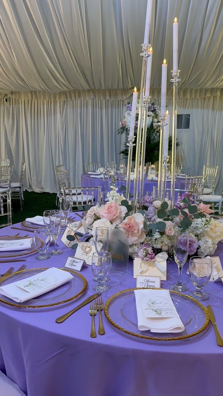 Lilac purple wedding table setting with gold accents and floral centerpieces in a tent.