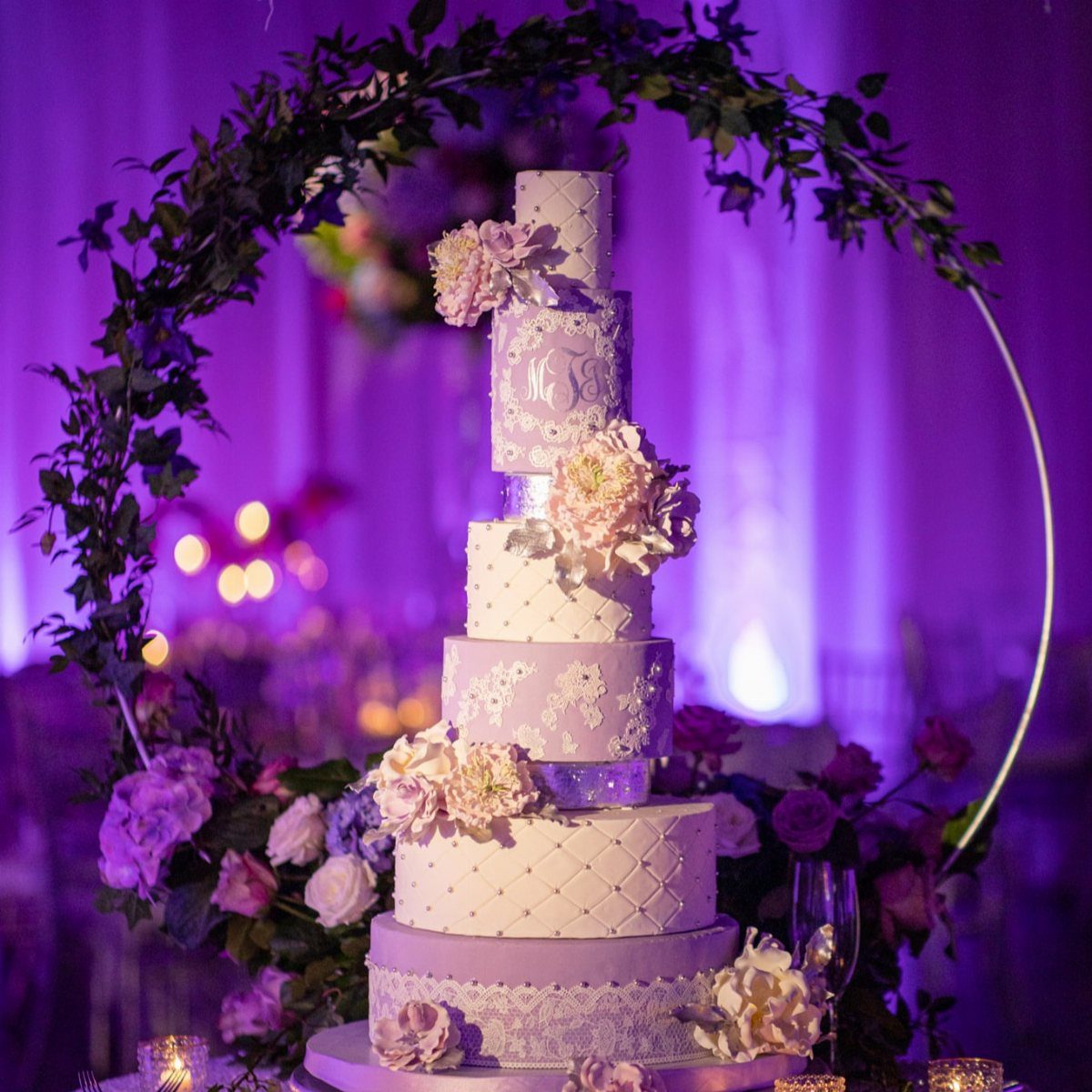 Multi-tiered lilac and white wedding cake decorated with flowers and lace patterns.