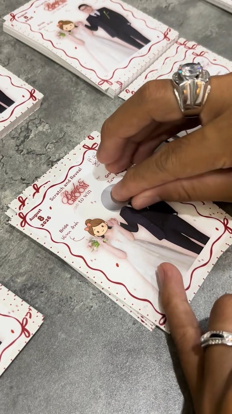 Hands scratching a custom wedding scratch card featuring a cartoon bride and groom.