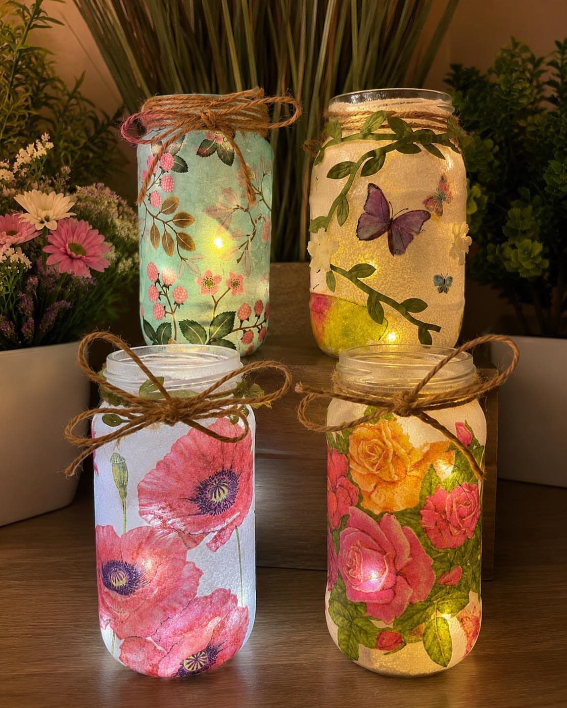 Four illuminated mason jars decorated with floral patterns and tied with brown twine.