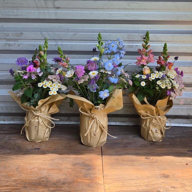 Three brown paper wrapped mason jars with colorful wildflowers on a wooden surface.