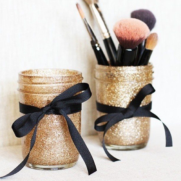 Gold glitter mason jars with black ribbons, one holding makeup brushes.