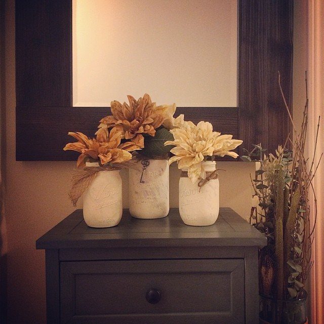 White painted mason jars with autumn flowers tied with brown jute string.