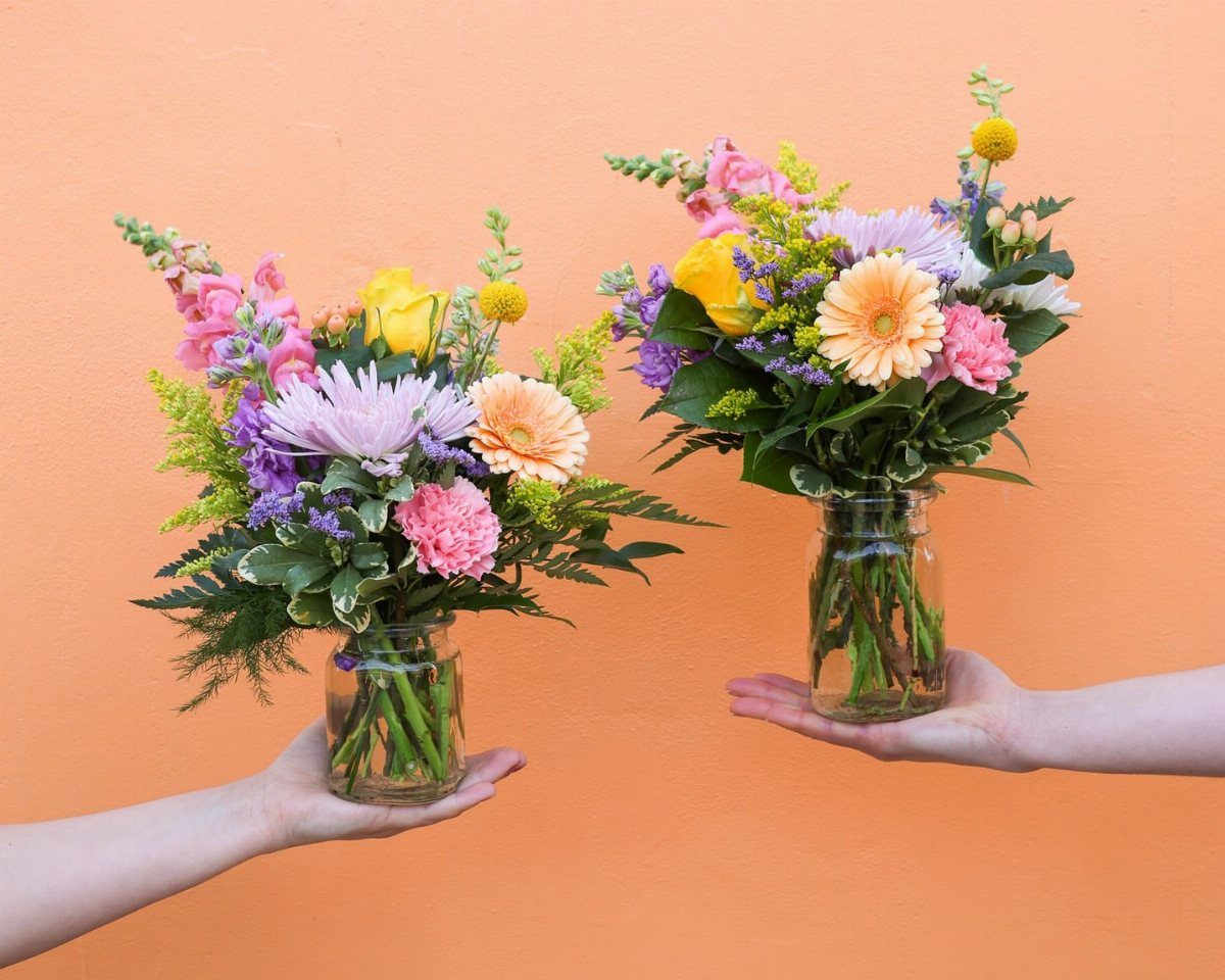 Two mason jars filled with colorful wildflowers held against a peach background.