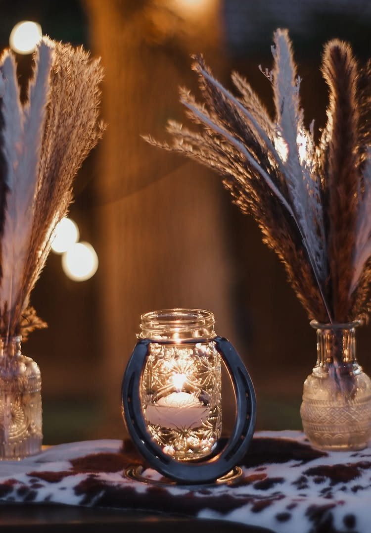 Mason jar candle encircled by a horseshoe on a cow-print table with pampas grass.