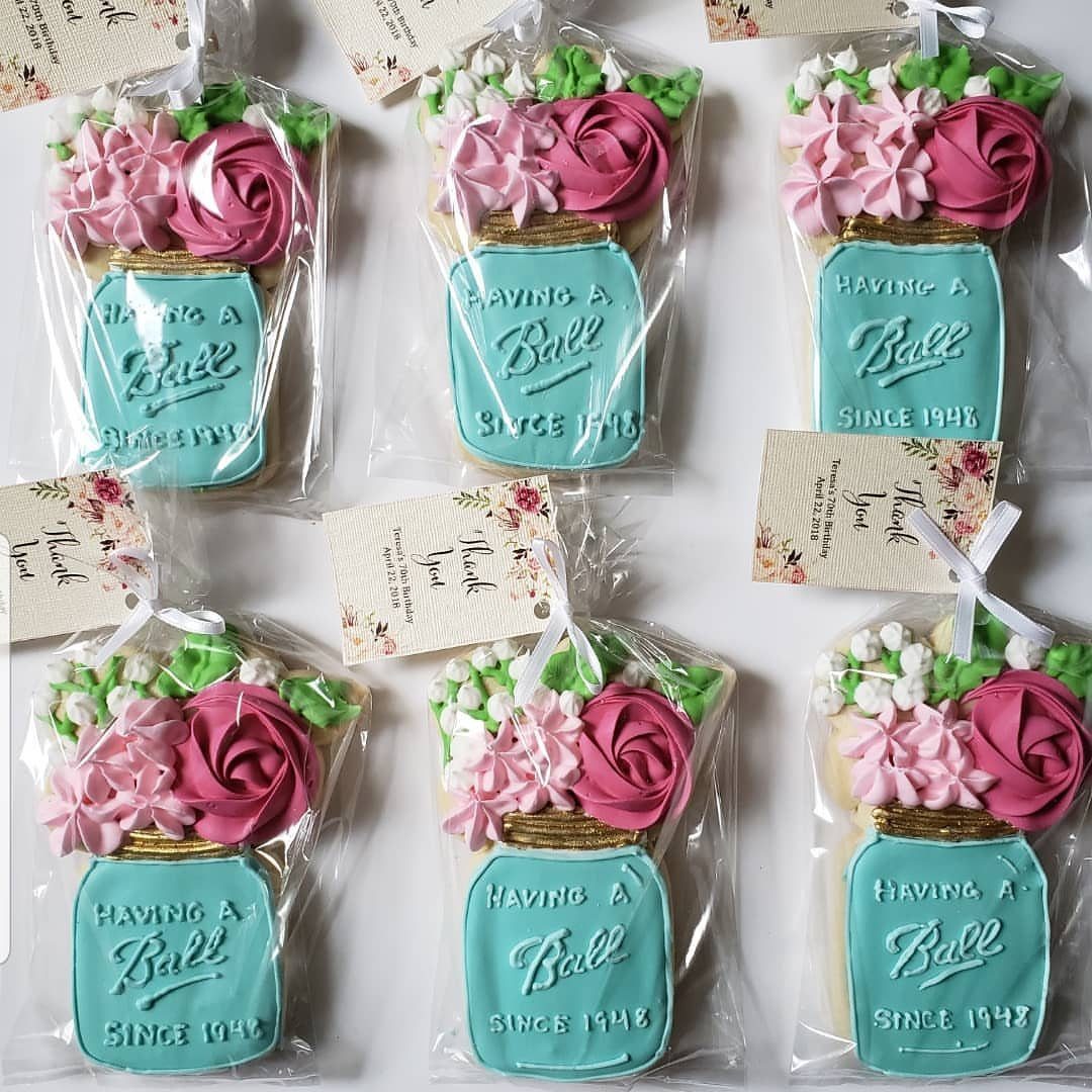 Sugar cookies shaped like turquoise mason jars with pink frosting flowers and tags.