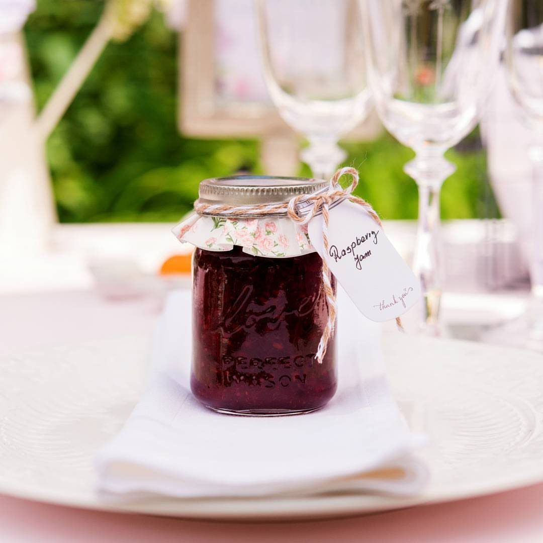 Mini mason jar of raspberry jam with floral fabric lid and gift tag