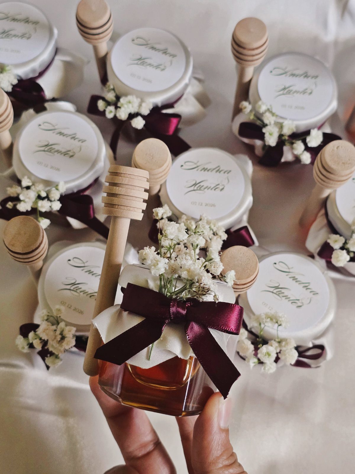 Small honey jars with personalized lids, burgundy ribbons, and baby's breath flowers.
