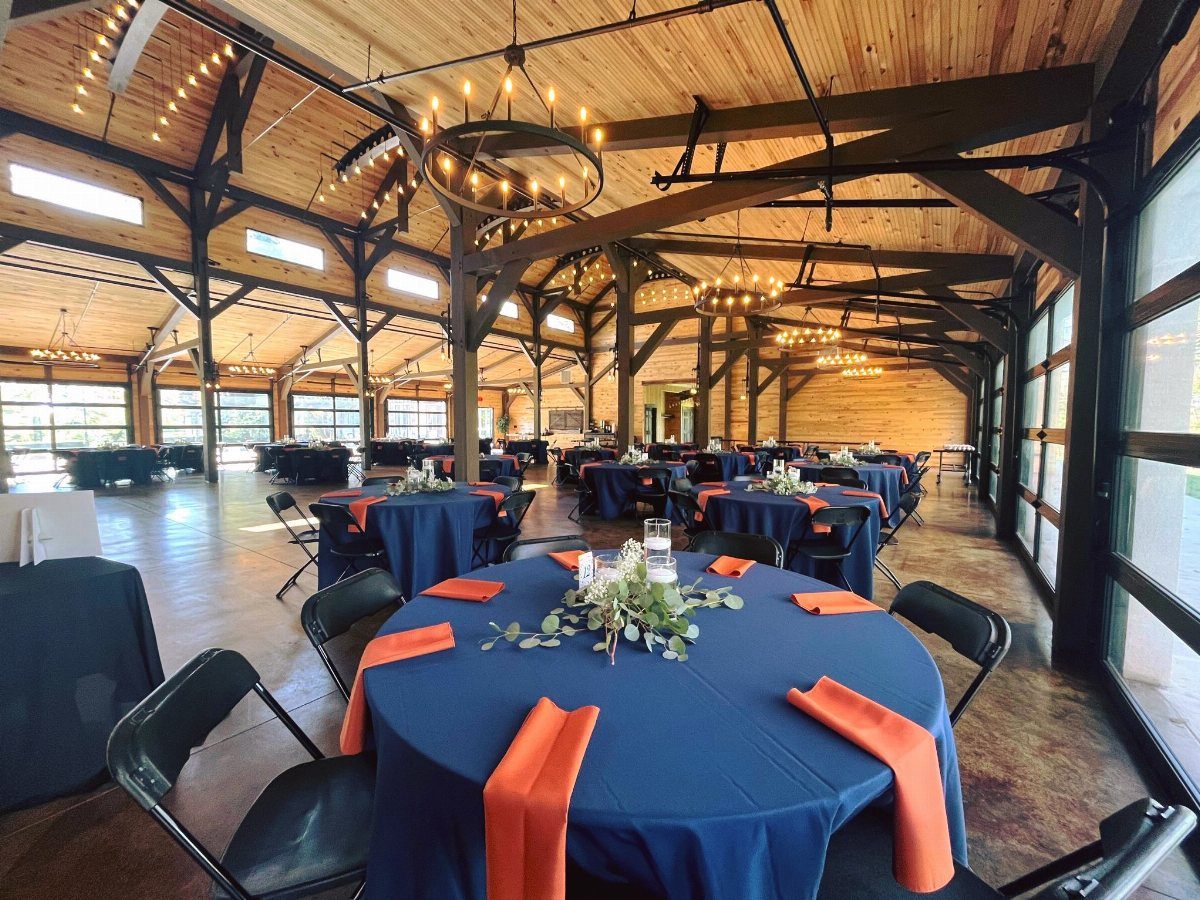 Navy blue tablecloths with burnt orange napkins in a rustic wooden event hall.
