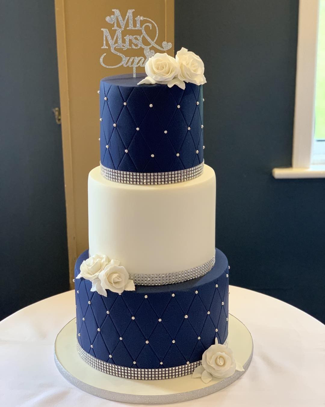 Three-tier wedding cake with navy blue quilted layers, white middle layer, and silver accents.
