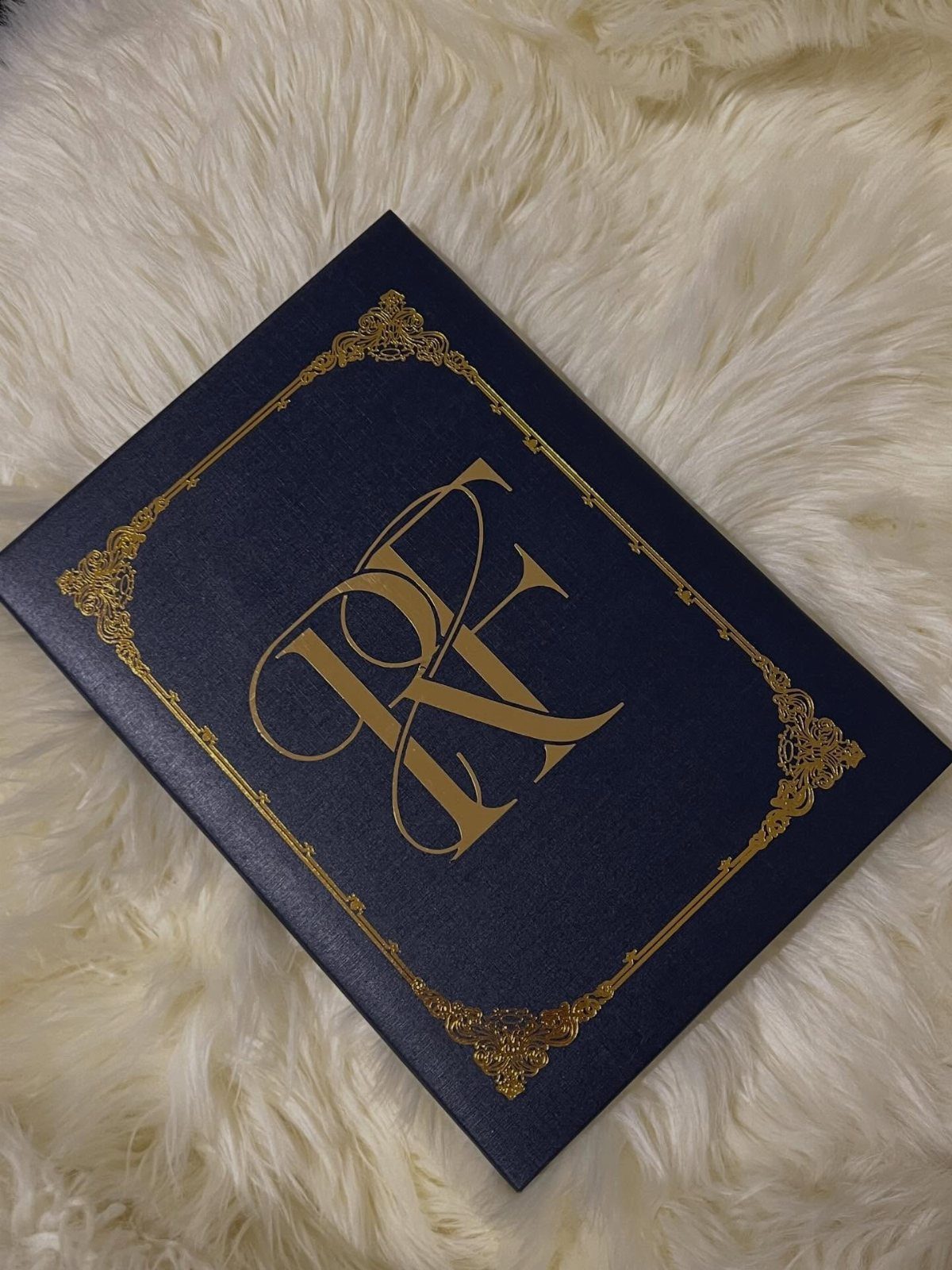 Navy blue guest book with gold foil monogram on white faux fur background