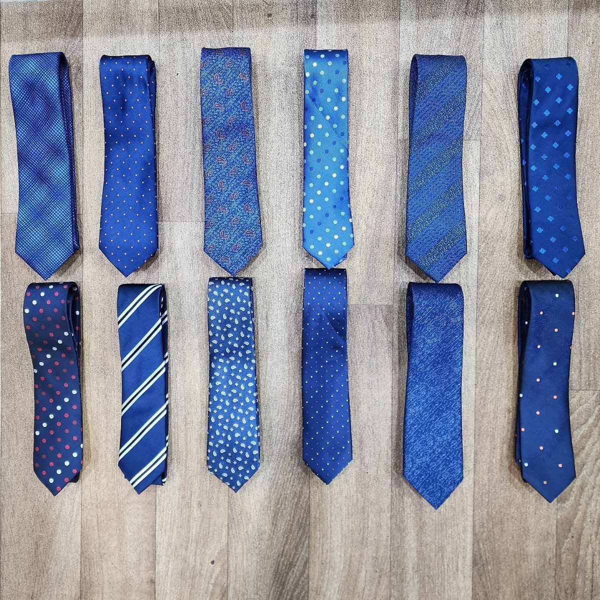 Twelve navy blue neckties with different patterns laid out on a wooden floor.