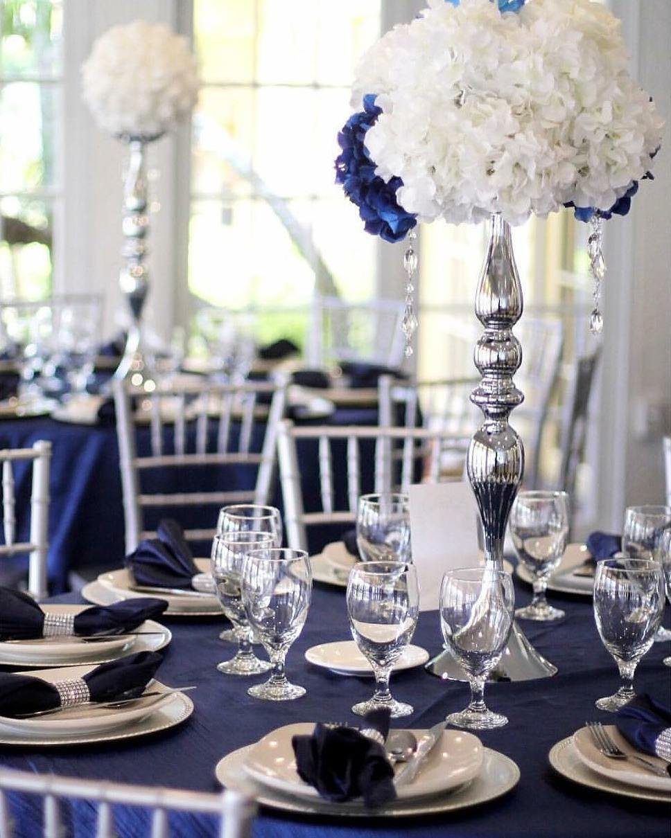 Navy blue tablecloth and silver chairs with white floral centerpieces on silver stands.