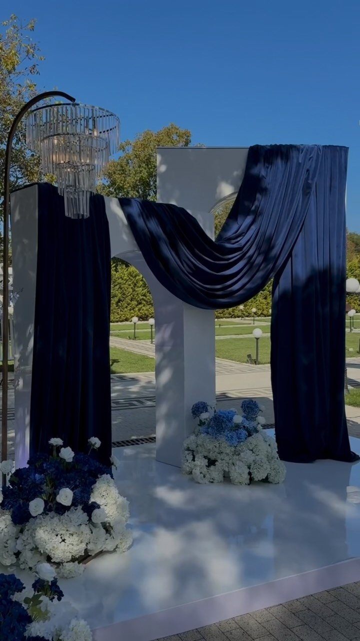 White wedding arch draped in navy blue fabric with blue and white floral arrangements.