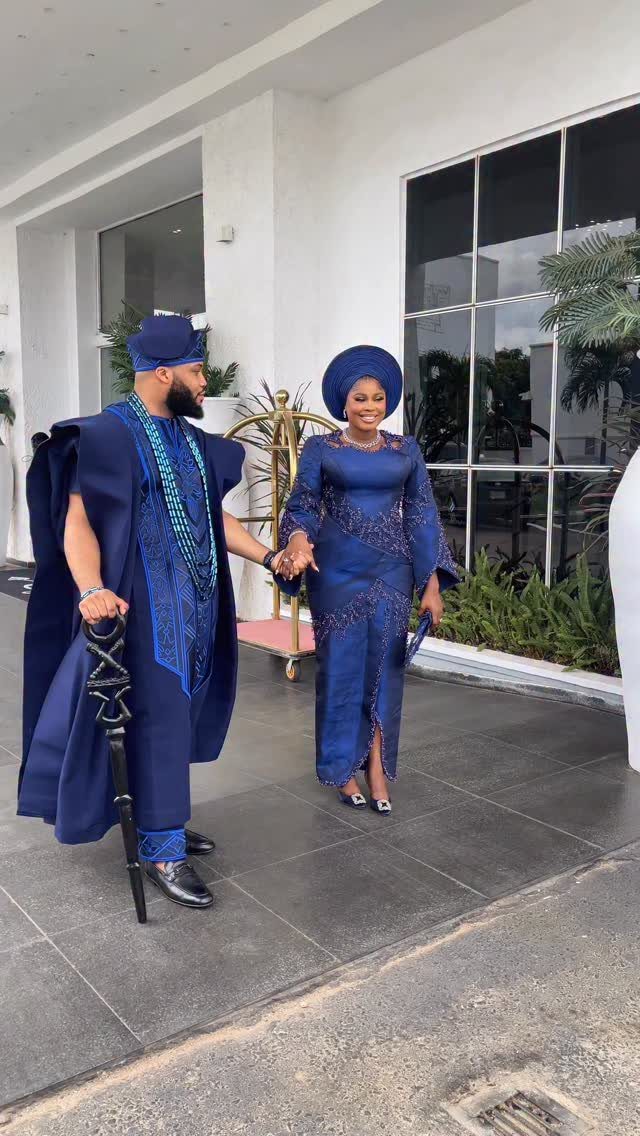 Couple in matching navy blue traditional Nigerian wedding attire holding hands outdoors.