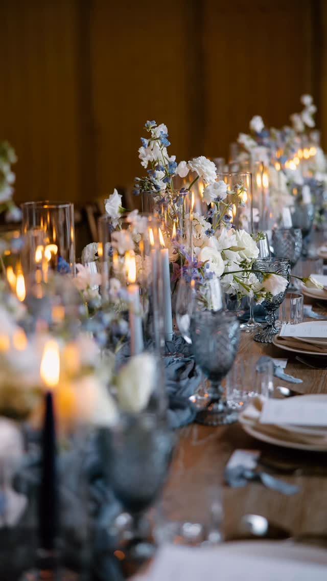 Wedding table setting with dusty blue and white flowers, candles, and blue glassware.
