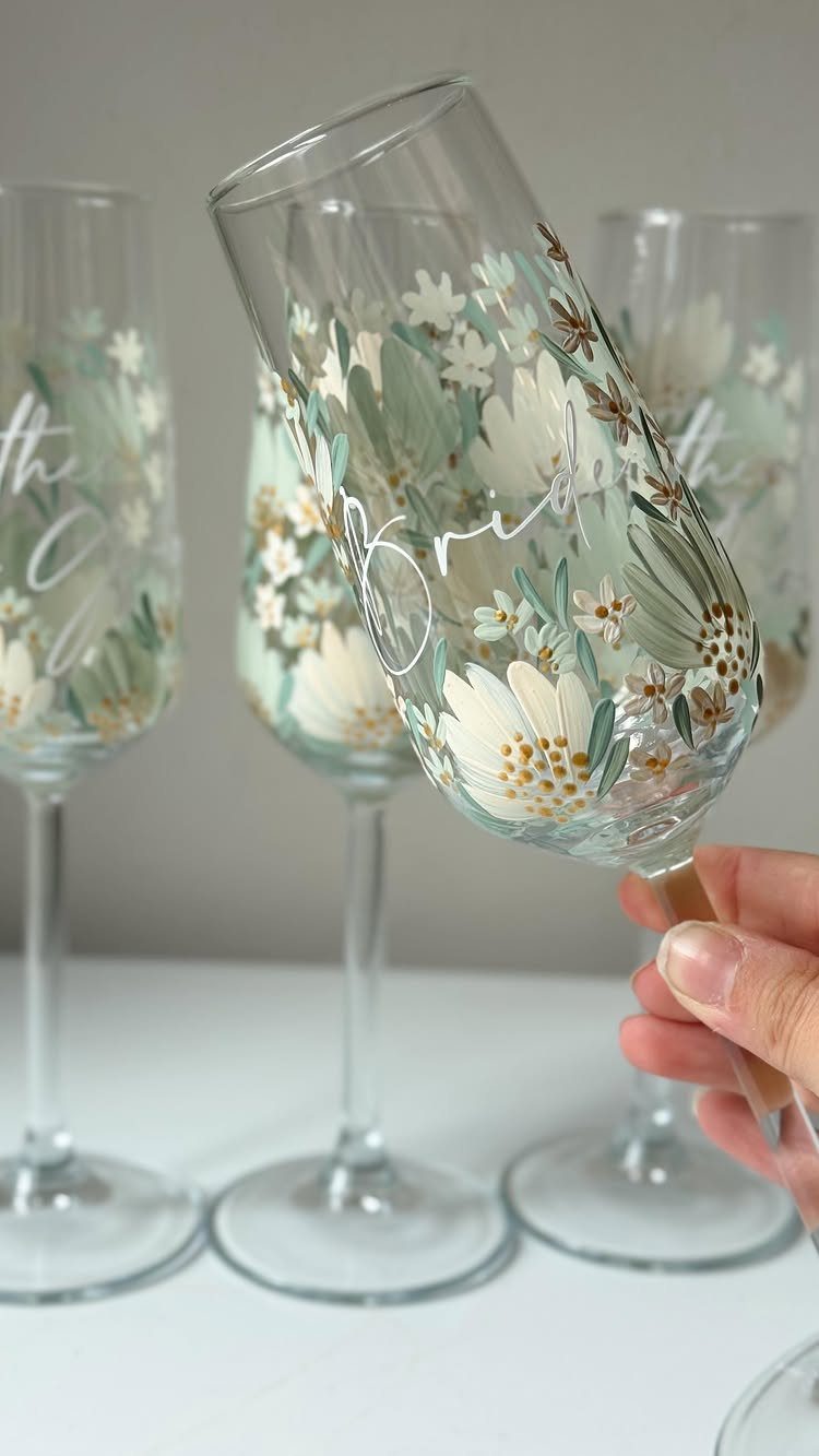 Champagne flutes decorated with white flowers and sage greenery for a bride.