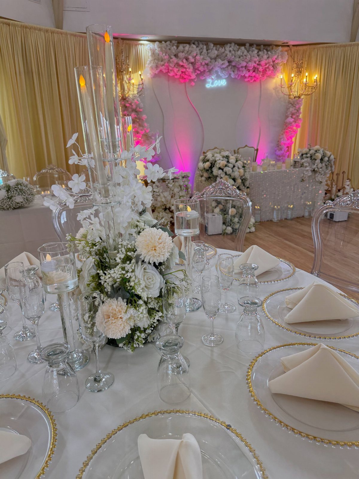 Ivory wedding table setting with gold-rimmed plates and white floral centerpieces.