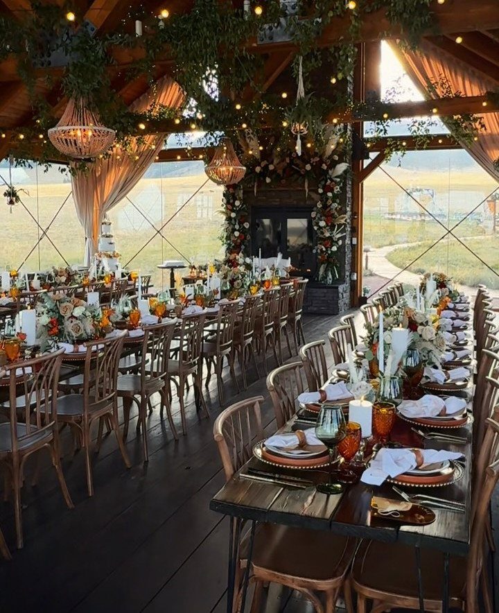 Rustic wedding reception with dark wood tables, amber glassware, and rust-colored floral arrangements.