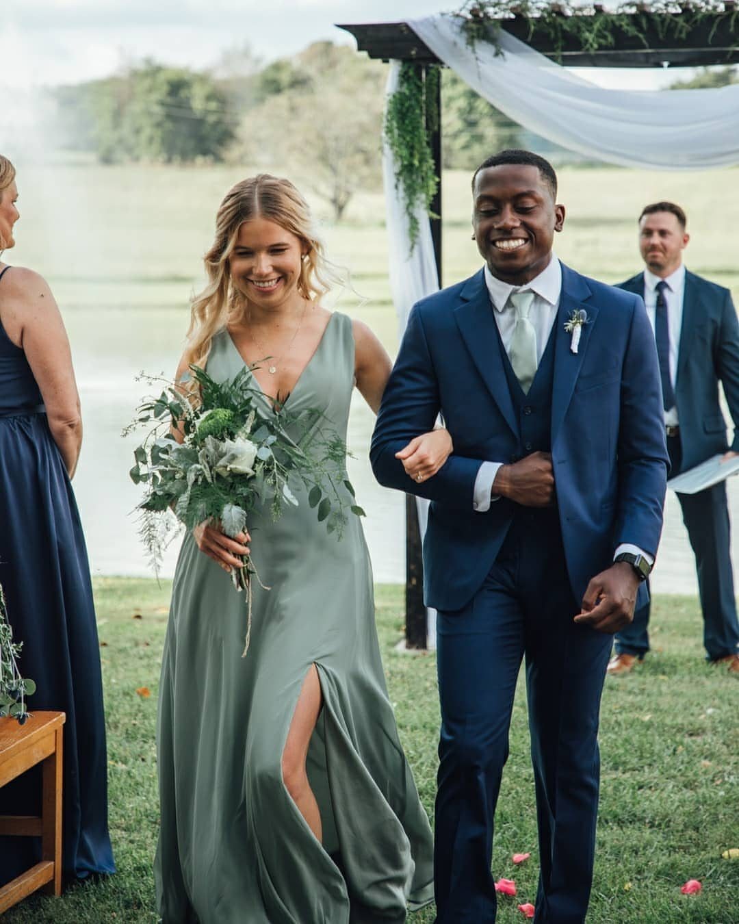 Couple walking at a wedding, woman in sage green dress, man in blue suit