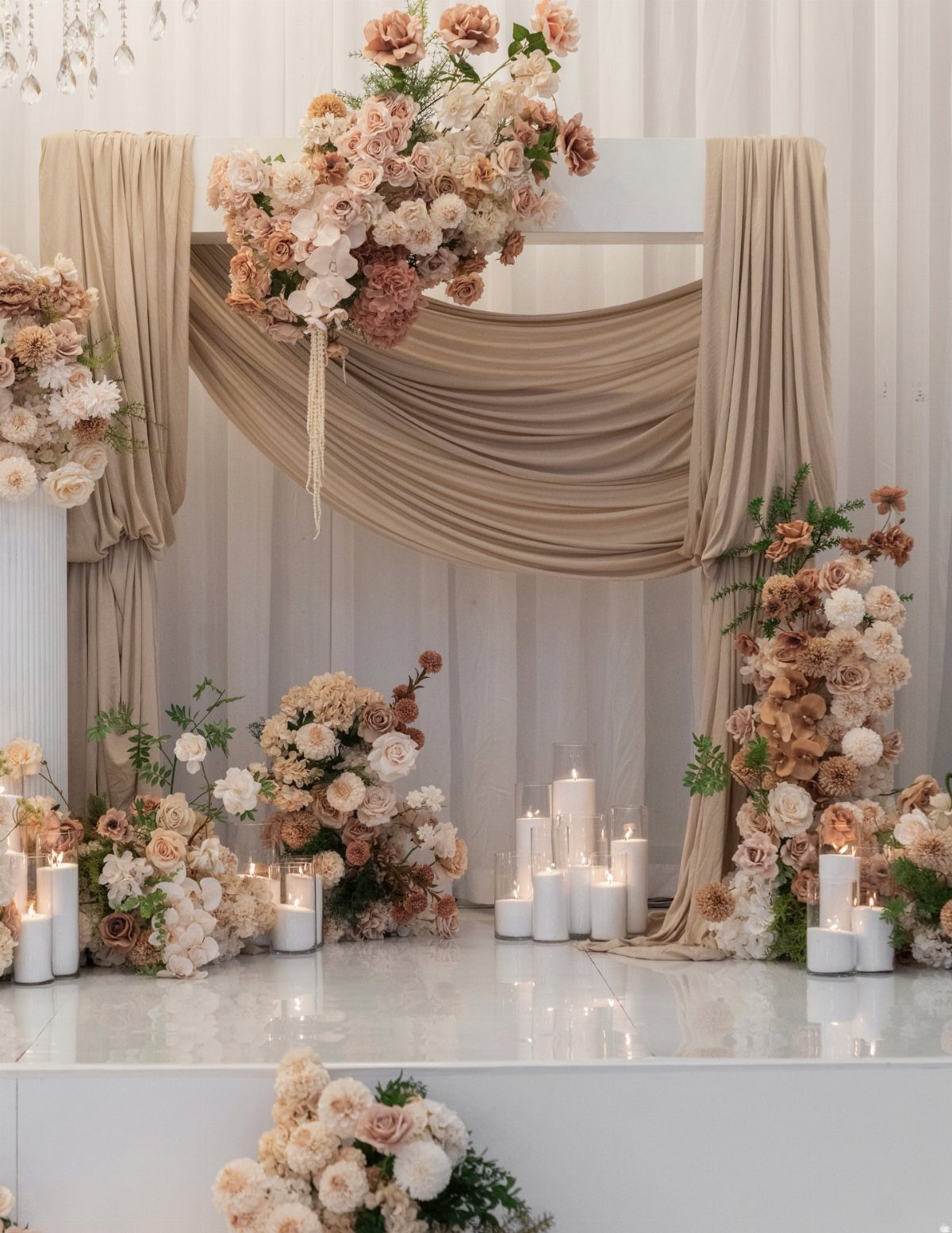 Beige draped wedding altar decorated with coral and cream flowers and white candles.
