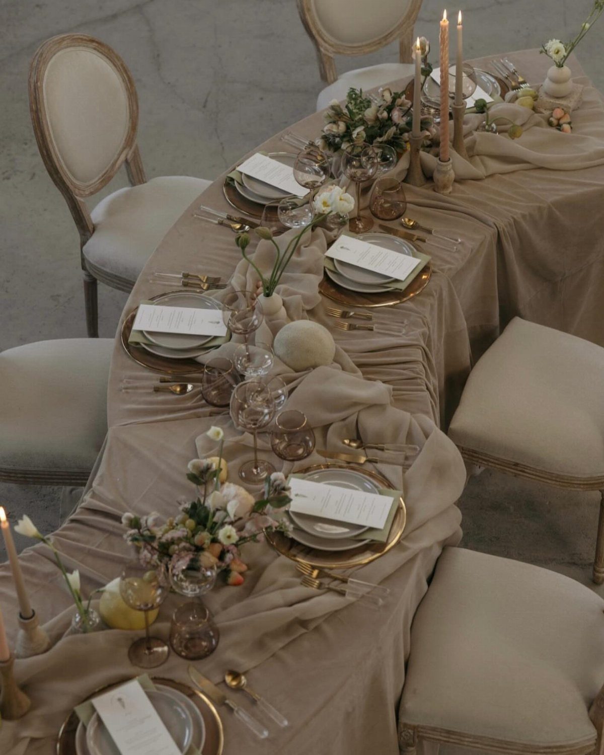 Taupe draped table linens with gold plates and white floral centerpieces for wedding.