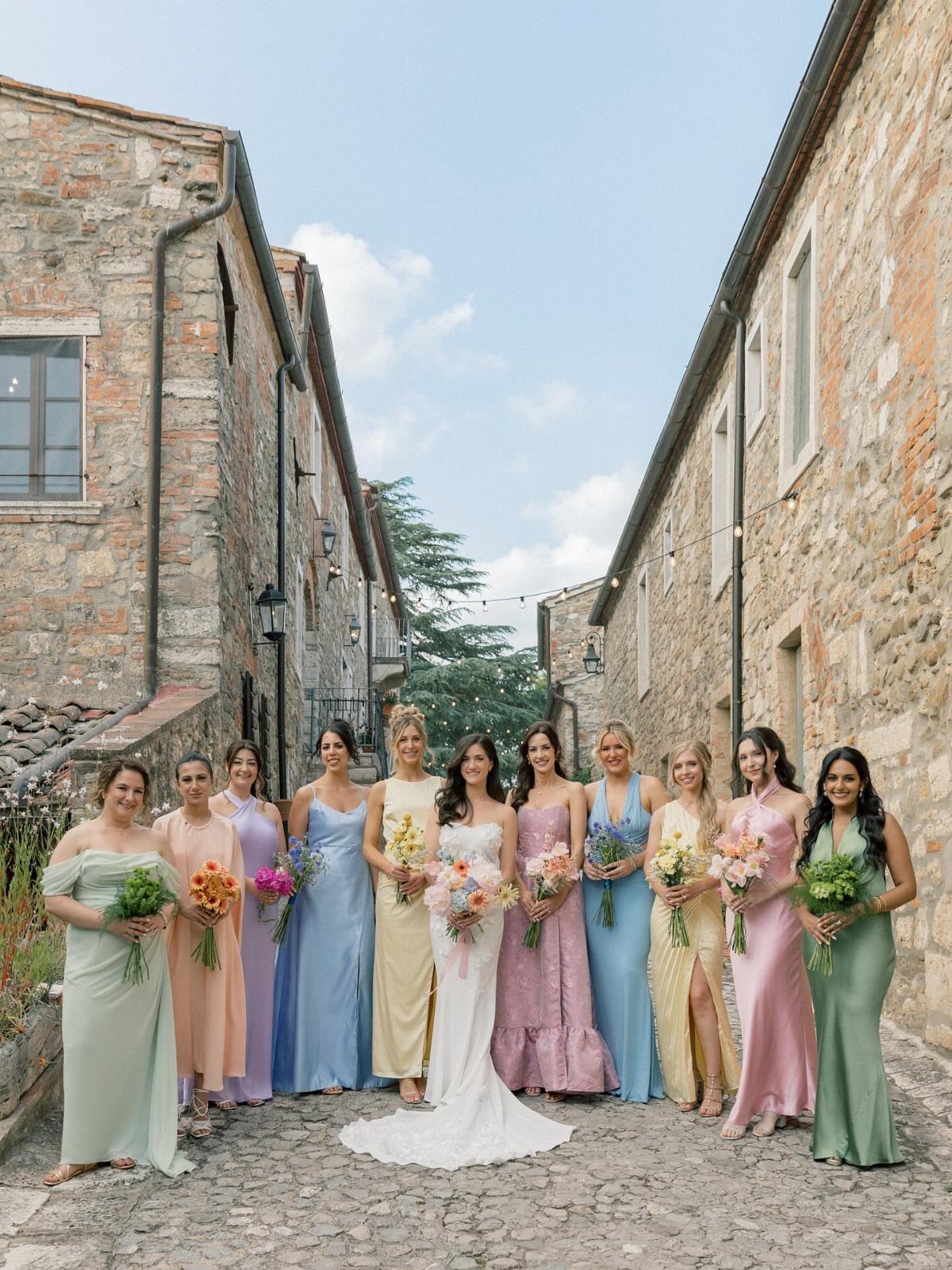 Bride and bridesmaids in a variety of pastel colored dresses on a cobblestone street