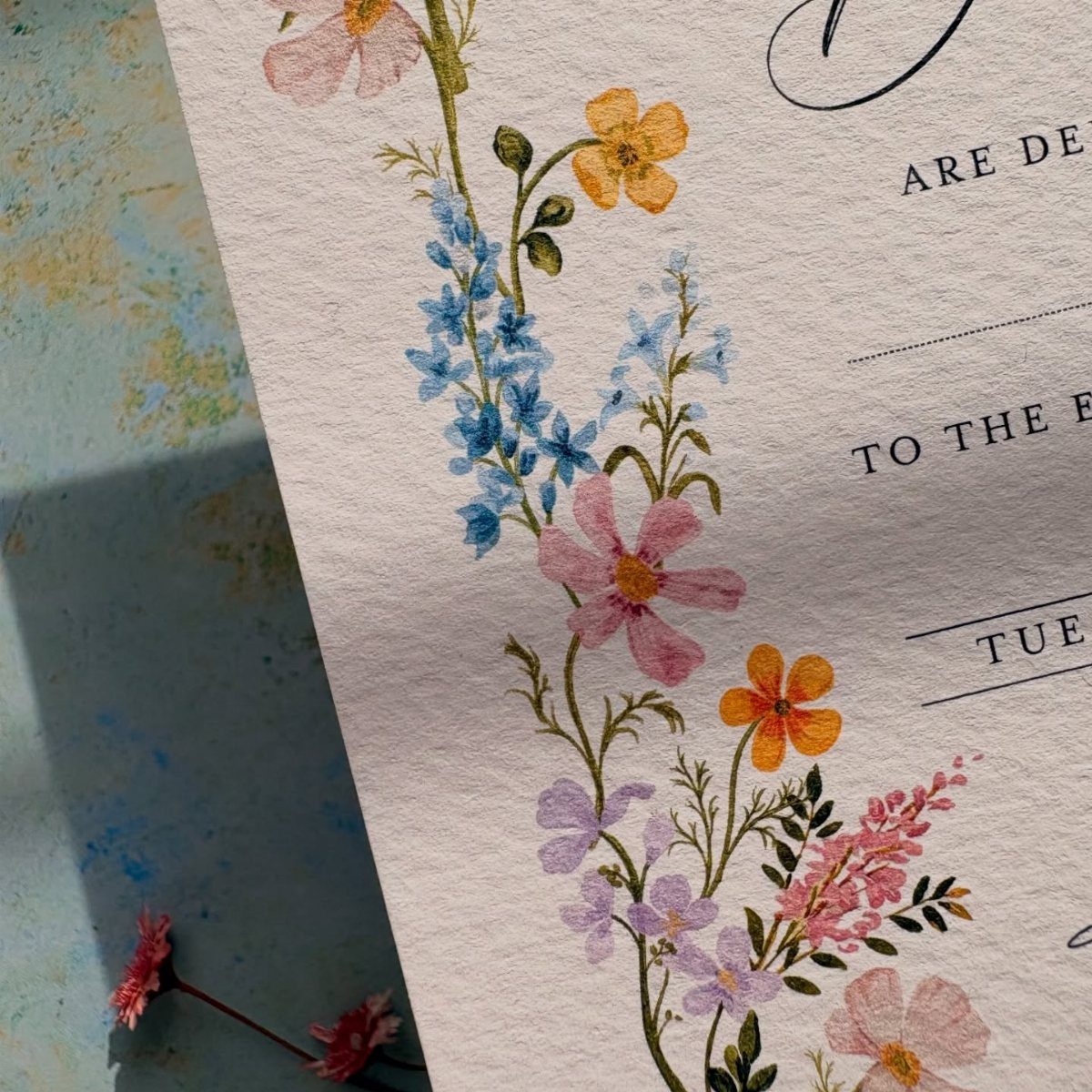 Wedding invitation with pastel watercolor flowers and elegant black typography on textured paper.