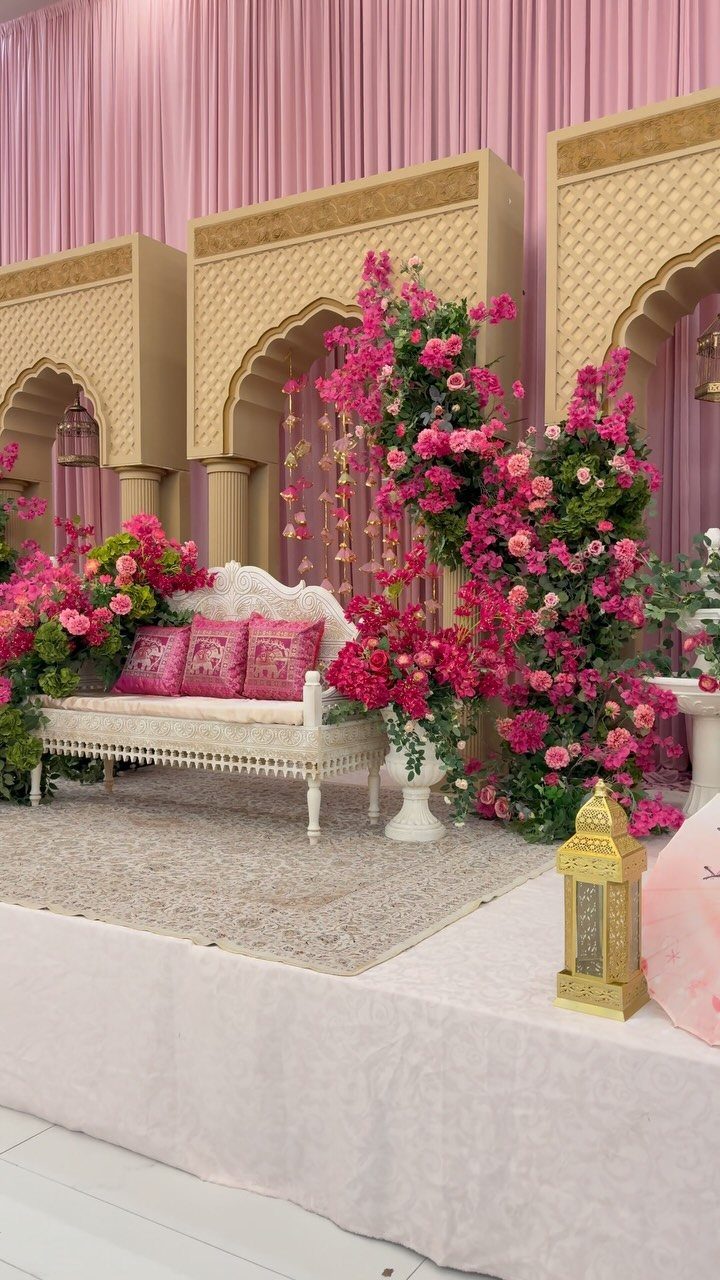 Ornate wedding stage with white sofa, pink floral arrangements, and gold arched backdrops.