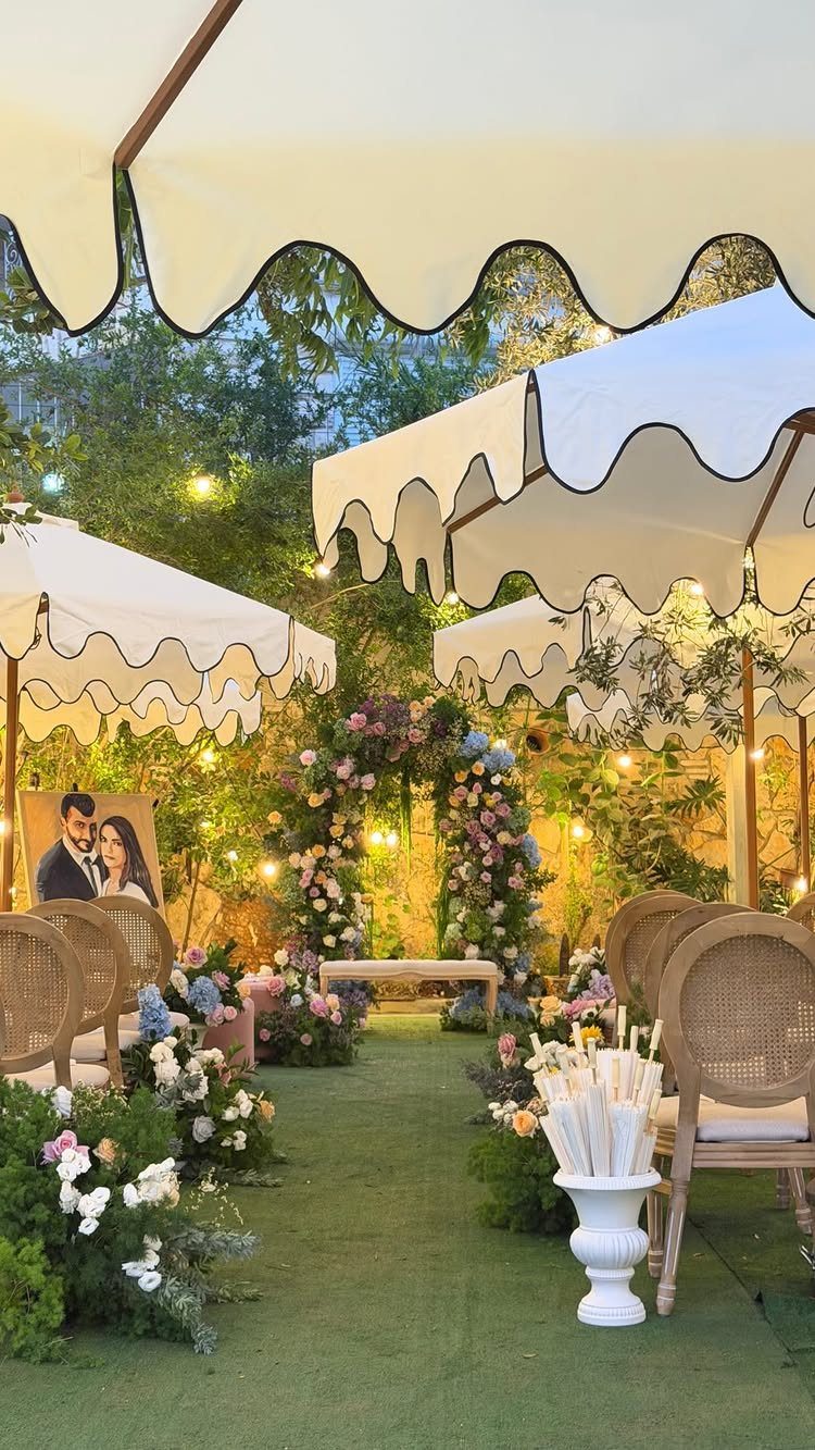 Outdoor wedding venue with white scalloped canopies, wicker chairs, and pastel floral arch.