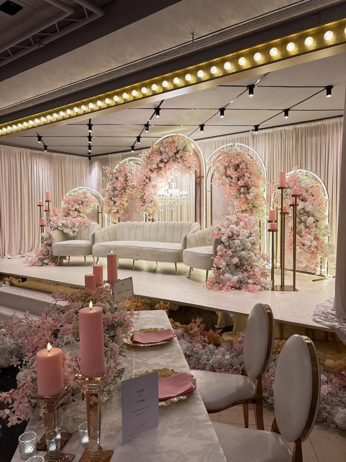 Pink pillar candles on a wedding table with floral arches and white sofa.