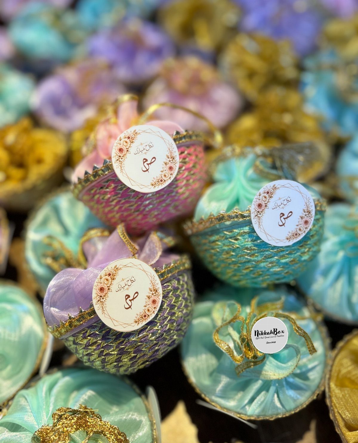 Pastel woven favor baskets in pink, blue, and purple with gold calligraphy tags.