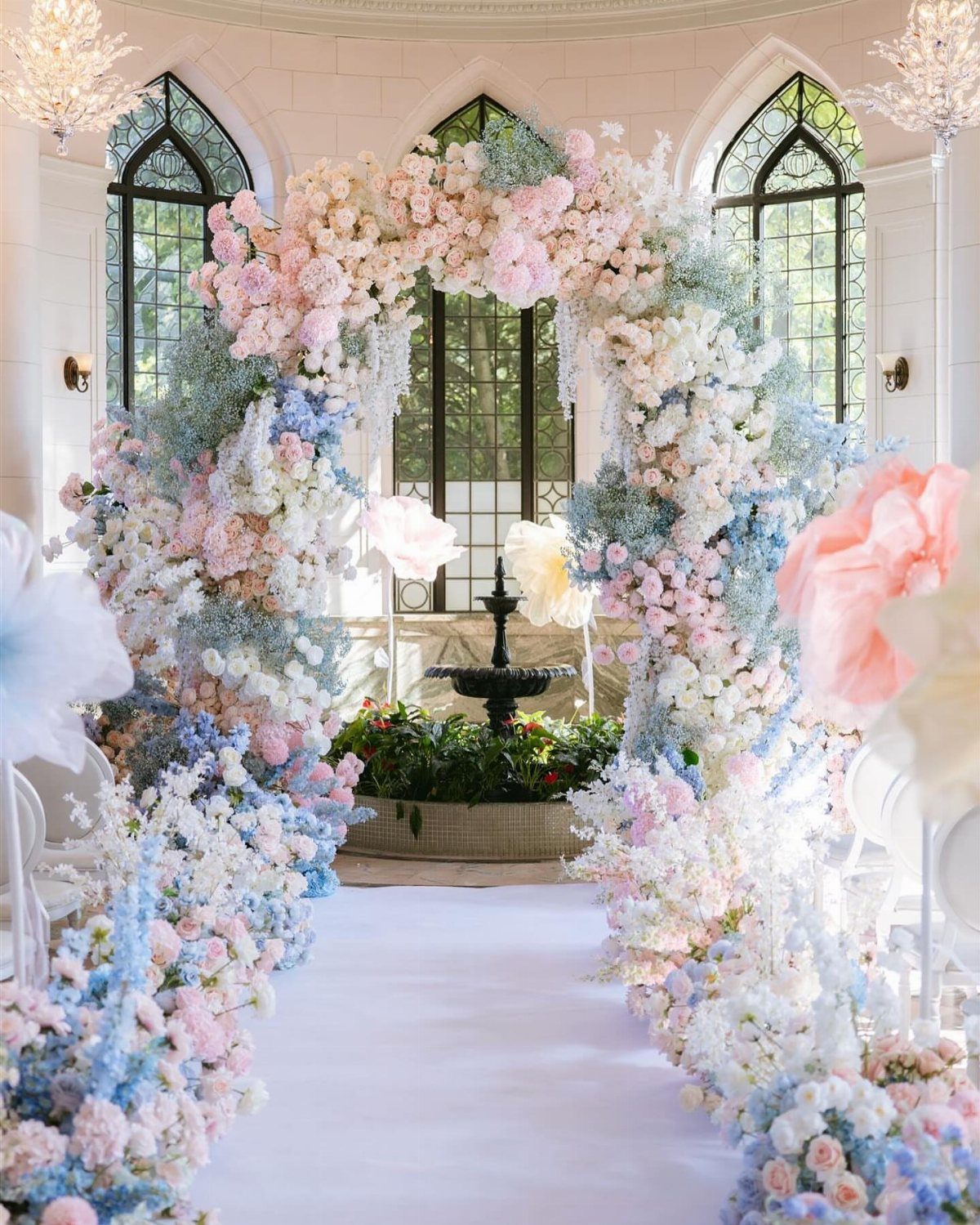 Wedding aisle with white runner and pink and blue floral arrangements and arch.