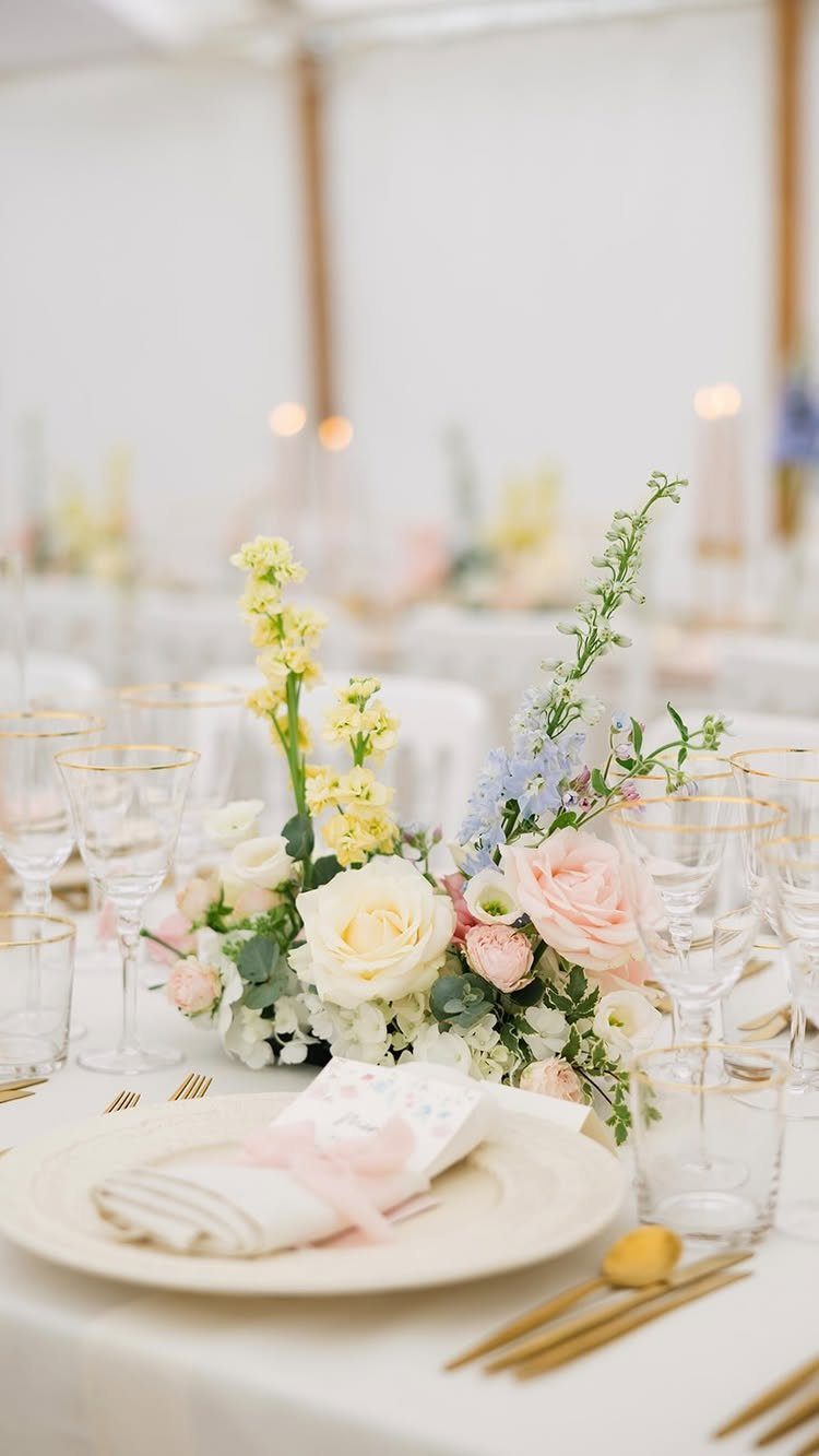 Wedding table setting with pastel pink and blue floral centerpieces and gold cutlery