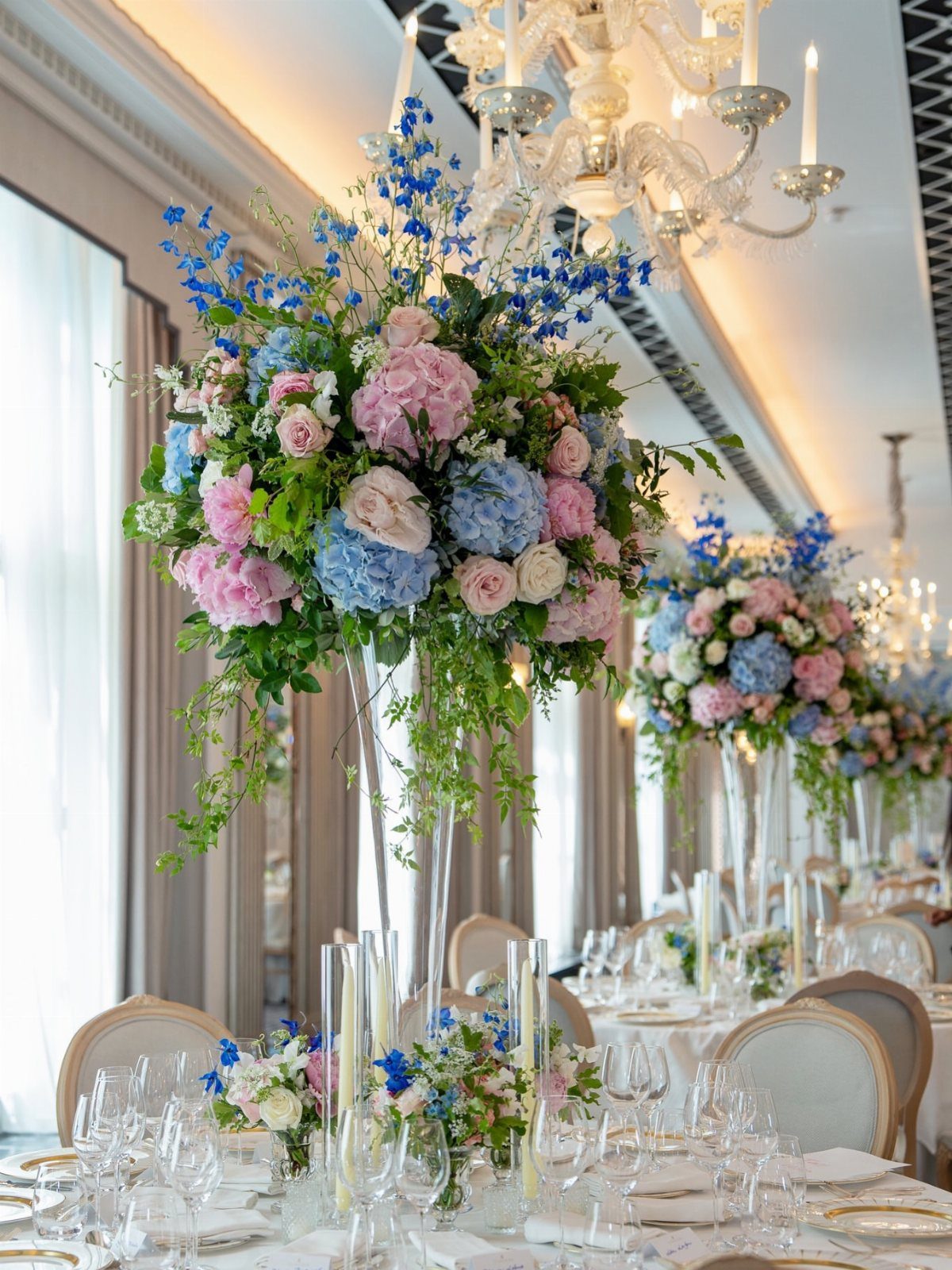 Pink roses and blue hydrangeas in tall glass vases on wedding tables